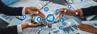 İki profesyonel, modern ofis ortamında takım çalışması ve stratejik planlamayı vurgulayarak, veri grafikleriyle çevrili bir hesap makinesi kullanarak KPI analizi üzerinde işbirliği yapmaktadır. Dostluk