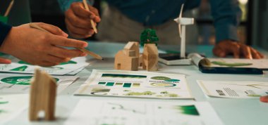 Bu resim, bir ekibin sürdürülebilir mimari, sergilenen modeller, çizimler ve bir masada çevre dostu kavramlara odaklandığı ortak bir tasarım oturumu yakalar. SACTR