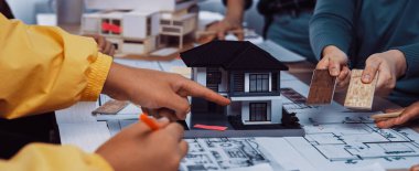 Çeşitli profesyonellerden oluşan bir grup, parlak bir ofis ortamında ev modeli, renkli malzemeler ve planlar kullanarak bir mimari tasarım projesi üzerinde işbirliği yapmaktadır. SACTR