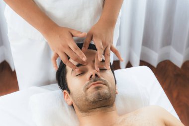 Beyaz adam stres önleyici kafa masajından ve lüks bir tatil beldesi veya otel spa salonundaki modern ışık ortamında yüz güzelliği eğlencelerini şımartmaktan hoşlanıyor. Sessiz.