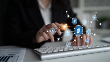 Çağdaş bir ofis alanında veri yönetimi ve teknolojiyi sembolize eden dijital simgelerle ilgilenen bir iş adamı, yenilik ve verimliliği ön plana çıkarıyor. Tessel