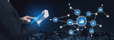 Bir işadamı dijital tablet ile etkileşime girer, ağ bağlantılarını ve grafikleri sergiler, kentsel bir gece ortamında veri analizi ve iş stratejilerini sembolize eder. Tessel