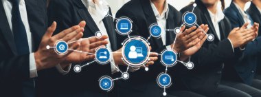 Profesyonel bir izleyici konferans sırasında, ağ oluşturma ve teknoloji entegrasyonunu sembolize ederek, kurumsal bir ortamda işbirliği ve bağlantı göstererek alkışlıyor. Dostluk