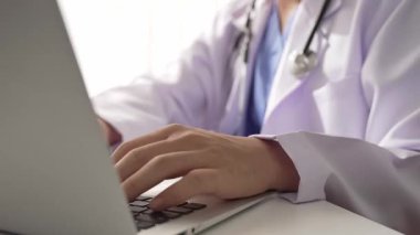 Hastanedeki doktor masasında oturup dizüstü bilgisayar üzerinde çalışıyor. Hasta test sonuçlarını teşhis ediyor, hastalıklar ve hastalıklar için tedavi planı geliştiriyor. Sağlık personeli ve sağlık hizmetleri. Ağır çekim. Katı.