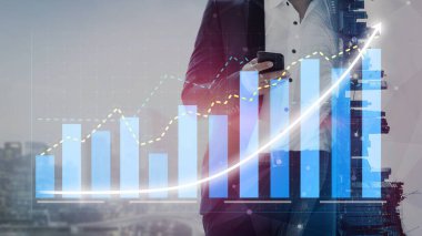 Takım elbiseli bir işadamı, kentsel bir ortamda finansal grafikleri ve verileri analiz ederken, modern iş eğilimleri ve analizleri gösteren bir akıllı telefon kullanır. Copula