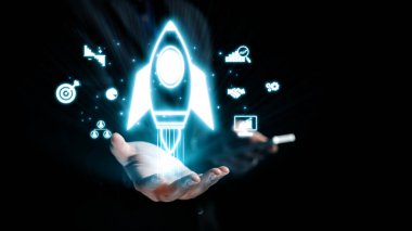 Bir el, çeşitli iş ve teknoloji simgeleri arasında yenilik ve büyümeyi sembolize eden, dijital gelişimin özünü gözler önüne seren parlayan bir roket ikonu sunar. Dörtgen