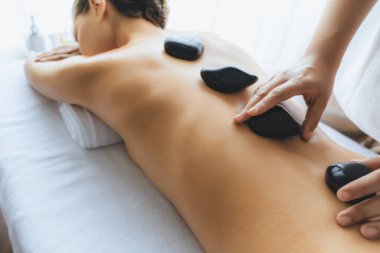 Lüks tatil köyündeki kaplıcalarda sıcak taş masajı. Gün ışığı sükunet ortamında, mutlu kadın müşteri bazalt taş masajından zevk alıyor. Rahatlatıcı bir sıcaklıkla vücudun üzerinde süzülüyor. Sessiz.