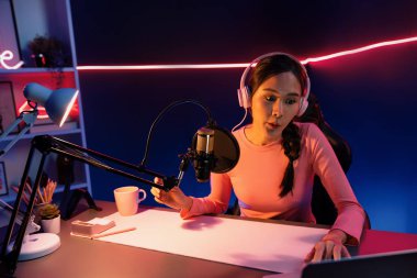 Geceleri podcast 'te olumlu konuşmalar yapan, pembe neon ışıklı modern stüdyoda sunum için dizüstü bilgisayar kullanan, gülümseyen, genç, güzel Asyalı bir etkileyiciydi. Taktik.