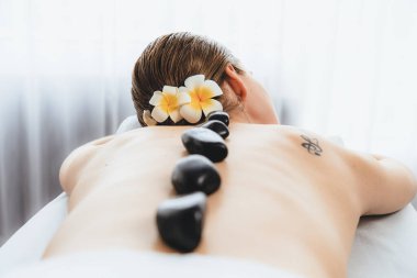 Lüks tatil köyündeki kaplıcalarda sıcak taş masajı. Gün ışığı sükunet ortamında, mutlu kadın müşteri bazalt taş masajından zevk alıyor. Rahatlatıcı bir sıcaklıkla vücudun üzerinde süzülüyor. Sessiz.