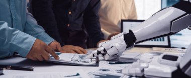 Veri analizi ve raporlama hazırlıklarında takım çalışmalarını vurgulayan, modern bir ofiste iş dünyasından profesyonellerle işbirliği yapan robotik bir eli gösteren fütüristik bir sahne. Noogenesis