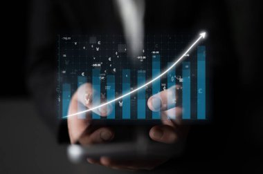 Bir iş adamı, yükselen bir grafiği gösteren akıllı bir telefon sunar, finansal büyüme ve şirket ortamındaki pazar analizini sembolize eder. Etki