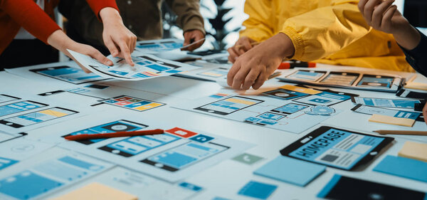 Живая группа креативных профессионалов работает над дизайном пользовательского интерфейса, размещая красочные прототипы и эскизы на столе, способствуя инновационным идеям и решениям. SACTR