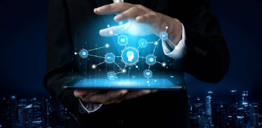 Takım elbiseli bir işadamı, fütüristik teknoloji simgeleri ve veri bağlantılarını canlı bir şehir manzarasına karşı sergileyen dijital bir tablet kullanıyor. Tessel