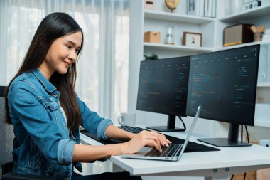 IT geliştiricisinde gülümseyen genç Asyalı dizüstü bilgisayarında kodlama programı verileriyle kotlu tişört giyerek çevrimiçi bilgi yazıyor. Güvenlik analizi iki ekran ile çevrili. Taktik.