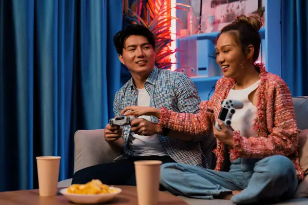 Neşeli, gülümseyen bir çiftin koltuğunda oturup oyun oynuyorlar. Oyun konsolu, hazır aperatifler ve içecekler, modern neon ışıklı, rahat oturma odasında eğlenceli bir rekabet seviyesinde. İnfobahn.