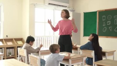 Beyazca öğretmeni, ilkokulda karatahta başında dururken vücut jesti kullanarak çok kültürlü öğrencilere teoriyi öğretiyor ve açıklıyor. Yetenekli öğretmen çocuklara soru soruyor. Pedagoji.