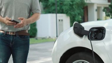 İlerici adam evindeki elektrikli aracın aküsüne emisyonsuz güç bağlantısı kuruyor. Elektrikli araç elektrik istasyonundan EV araba aküsüne kabloyla şarj oluyor.