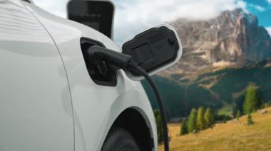 Temiz çevre için temiz enerjinin yol açtığı ilerici elektrikli araba kavramının arka planı olarak dağın tepesinde bulutun zaman kavramının yer aldığı doğal manzara. EV araba şarj istasyonunda şarj oluyor..