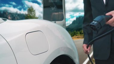 İş dünyasındaki yenilikçi adam elektrikli arabasını dağlarla dolu bir kırsal kesimdeki şarj istasyonundan alıyor. Yol yolculuğu, EV arabalı macera yenilenebilir enerjiyle çalışıyor..