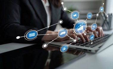 Bir iş adamı, analitik, büyüme ve çevrimiçi iletişim teknolojilerini sembolize eden dijital simgelerle çevrili modern ofis ortamında dizüstü bilgisayarla uğraşır. Tessel