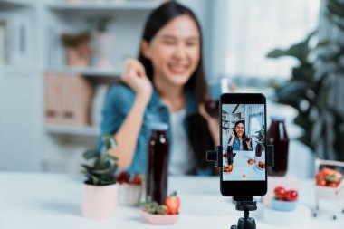 Seçici odaklı akıllı telefon ve gülümseyen genç, güzel Asyalı karışık çilek ve kiraz suyu detoksu değerlendirmesi sosyal medyada sağlıklı ürün tanıtımı sunuyor. Taktik.