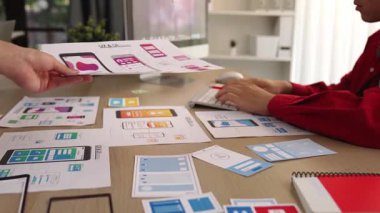 Mobil uygulama için kullanıcı arayüzü prototipini ofis çalışanlarına sunan harika bir şirket çalışanı. UX UI tasarımcısı kağıt üzerinde simge tasarımının işlevini açıklıyor. Sinerjik