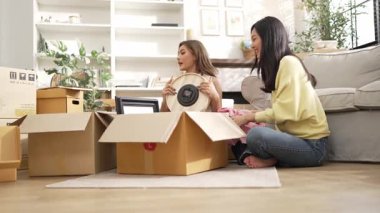 Kutudan kitap seçen ve oturma odasında kitap okuyan mutlu lezbiyen çift. Taşınırken kutular ve mobilyalarla çevrili otururken çekici bir kız konuşuyor ve paketleri açıyor. Yer değiştirin. Myrmidon.