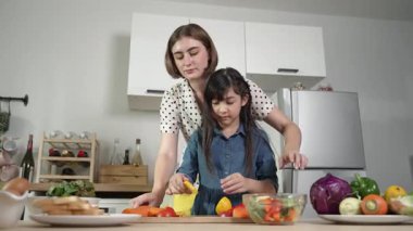 Zeki beyaz anne ve Asyalı kız birlikte yemek pişiriyor ve sebze doğruyor ya da akşam yemeği için salata hazırlıyor. Mutlu anne ve kız taze yemekle sağlıklı yemek yapıyorlar. Sağlıklı gıda konsepti. Pedagoji.