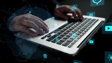 Modern çalışma alanında teknoloji ve iletişim kavramlarını gösteren dijital simgelerle geliştirilmiş bir dizüstü bilgisayarın klavyesine yazı yazan ellerin yakın çekimi. Xenic