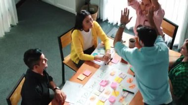 Yaratıcı başlangıç ekibinin takım çalışmalarını veya başarılı projelerini teşvik etmek için beşlik çakarken, aynı zamanda not ve yapışkan notlar kullanarak iş akışını yönetmek için yoğun bir görev tahtası yapmasının en üst görünümü. Cemaat.