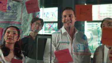 Cam duvarda yaratıcı fikirleri paylaşmak için renkli yapışkan notlar kullanarak pazarlama fikrini değerlendiren mutlu profesyonel iş adamları. Bir grup farklı iş adamları strateji hakkında tartışıyorlar. Yönlendirici.