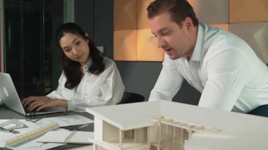 Ev planı çizmek için birlikte çalışan yetenekli mimar mühendisi. Mimar takımı, mimari model, plan ve dizüstü bilgisayarla ofis masasına yerleştirilen ev inşaatı hakkında tartışır. Yönlendirici.