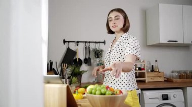 Kafkasyalı anne, modern mutfakta dizüstü bilgisayarda yemek tarifine bakarken salata yapmak için yemek hazırlıyor. Yetenekli ev bekçisi taze sebze kullanarak kahvaltı hazırlıyor. Pedagoji.