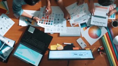 Tasarımcı fikirleri yazarken proje yöneticisinin yukarıdan aşağıya bakan görüntüsü. Akıllı iş adamları logo tasarımı fikrini açıklarken tasarımcılar palete bakarken temayı seçiyorlar. Sempozyum.