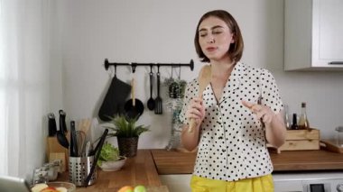 Enerjik beyaz anne kahvaltı için salata pişirirken ve yemek pişirirken elinde kepçeyle şarkı söylüyor. Sağlıklı yemek yapmaya hazırlanırken müziğe yönelen mutlu ev sahibi. Pedagoji.