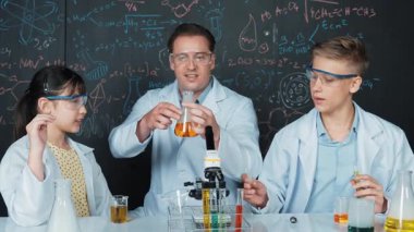 Zeki kız, çeşitli öğrenciler STEM fen dersinde deney yaparken renkli sıvıyı inceliyor. Bir grup liseli çocuk tahtada dururken laboratuvarda çalışıyor. Yaratıcı. Öğretim