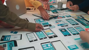 Çeşitli bir ekip, yenilikçi tasarım fikirleri ve işbirliği çabalarını sergileyen akıllı telefon ve tablet modellemeleriyle çevrili yaratıcı bir beyin fırtınası oturumuna girişiyor. SACTR