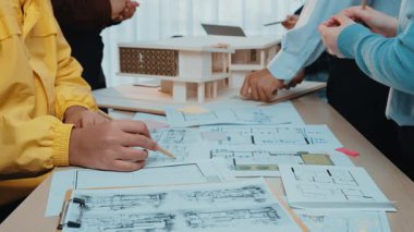 Mühendisler ve mimarlar, stratejik planlama ve yenilikçi tasarım tartışmaları içeren planlar, çizimler ve modellerle dolu bir masa etrafında işbirliği yaparlar. SACTR