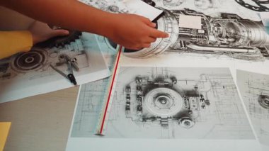 Bir mühendislik çalışma alanındaki detaylı teknik planları ve bileşenleri analiz eden ellerin yakından görüntüsü, makine tasarım ve geliştirme sürecini gösteriyor. SACTR