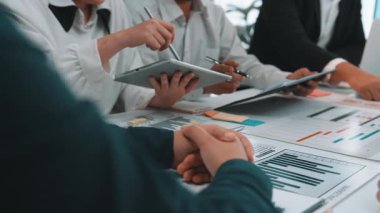 Çeşitli bir iş ekibi, verileri analiz ederek ve proje sunumu üzerinde strateji oluşturarak, takım çalışmalarını ve teknolojik bütünleşmeyi vurgulayarak, işbirlikçi bir toplantıya katılıyor. SACTR