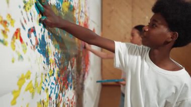 Çeşitli çocukların renkli duvarları eliyle boyadığı site manzarası. Çekici bir lise öğrencisi renk paletini tutarken duvarı el iziyle boyuyor. Yaratıcı aktivite. Öğretim