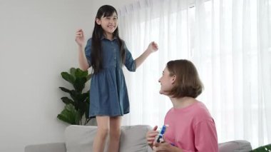 Annem gitar çalıp kıza bakarken yetenekli kız kanepede dans edip zıplıyor. Beyaz anne, çocuk oturma odasında dururken akustik müzik çalar. Aile eğlence konsepti. Pedagoji.