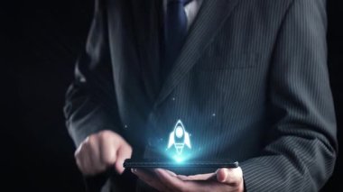 Resmi bir takım elbiseli bir işadamı, canlı bir roket ikonu ve çeşitli dijital semboller gösteren, yeniliği, büyümeyi ve başlangıç yolculuğunu sembolize eden bir akıllı telefon tutuyor. Dörtgen