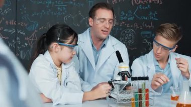 Zeki öğretmen, çeşitli öğrencilerin yaratıcı eğitim üzerine yazılmış bilim teorisiyle karatahta önünde deney yaparken test tüpü masanın üzerine yerleştirilirken mikroskop altında bakar.