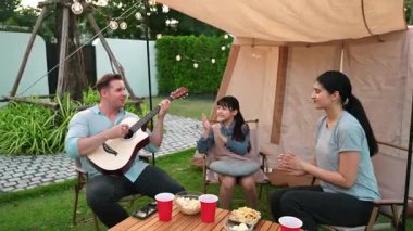 Baba gitar çalarken anne ve kız birlikte kampta oturuyorlar. Ebeveynler, genç nesil çapraz kuşak farklılıklarıyla zaman geçirmek için açık hava kamp aktivitelerini kullanıyorlar. Uyumsuzluk.