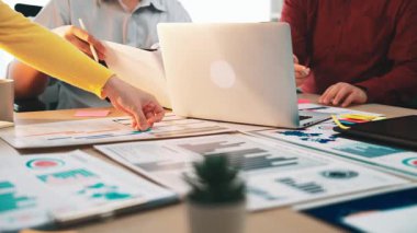 Bir grup iş adamı, modern ofis ortamında yaratıcılıkla dolu bir dizüstü bilgisayardaki çizelge ve belgeleri analiz ederek ortak bir tartışmaya giriştiler. SACTR