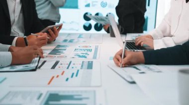 Profesyonel bir grup, dizüstü bilgisayar ve tabletlerde gösterilen çeşitli veri görselleştirmelerini aktif olarak tartışarak ve analiz ederek dinamik bir iş toplantısı yapar. SACTR