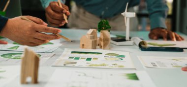 İşbirlikçi bir ekip, modern ofis ortamında yeşil kavramları ve yenilikçi fikirleri grafikler ve ahşap modellerle analiz ederek sürdürülebilir bir tasarım projesine girişir. SACTR