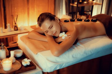 Lüks tatil köyündeki kaplıcalarda sıcak taş masajı, sıcak mum ışığı, spa bazalt taşı masajının keyfini çıkaran mutlu kadın müşteriler, rahatlatıcı bir sıcaklıkla vücudun üzerinde süzülüyorlar. Sessiz.
