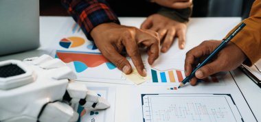 Masada görsel grafiklerle veri analizi yapan iki kişi, yaratıcı bir çalışma ortamında modern teknikler ve araçlar sergiliyor. Noogenesis